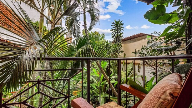 A balcony with a wooden chair, surrounded by lush tropical plants and a metal railing. - Studio Romantique – Your Tropical Hideaway in Historic Puerto Vallarta (Puerto Vallarta)