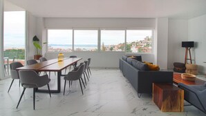 A modern living room with a large window, a dining area, and a sofa.
