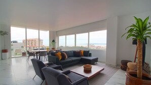 A spacious living room with a large sectional sofa, a coffee table, and a view of the city through large windows.
