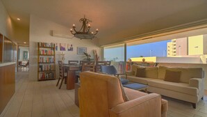 A spacious living room with a large window, a chandelier, a bookshelf, and a sofa.