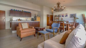 A modern living room with a sofa, chairs, a coffee table, and a kitchen area with cabinets and appliances.