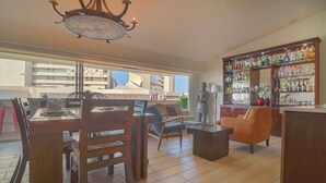 A spacious living area with a dining table, chairs, a sofa, and a bar area with shelves of bottles.