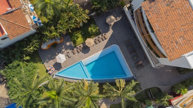 An aerial view of a resort with a swimming pool, palm trees, and tiled roofs.