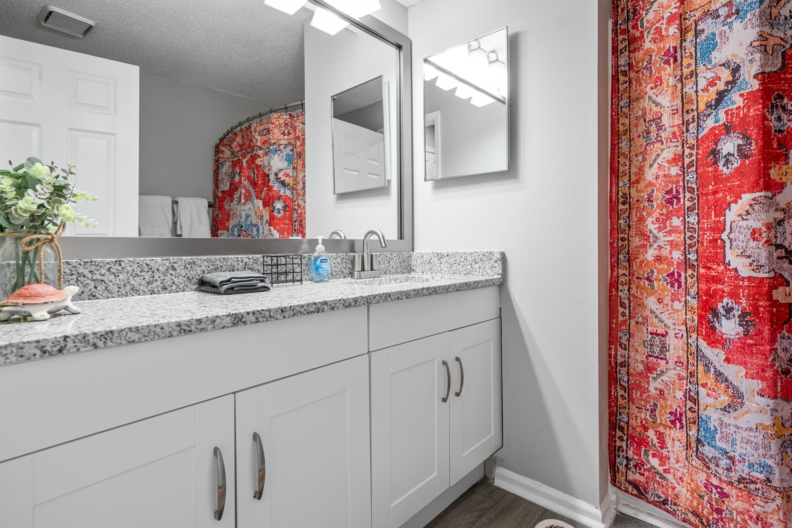 A bathroom with a white vanity, a mirror, and a shower curtain with a floral pattern.
