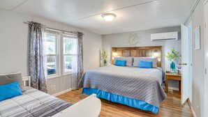 Une chambre à coucher avec un grand lit, un plus petit lit, une table de chevet, une fenêtre avec des rideaux et un appareil de climatisation.
