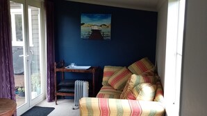 A cozy room with a sofa, a small table, and a radiator. There is a window with curtains, and a painting on the wall.