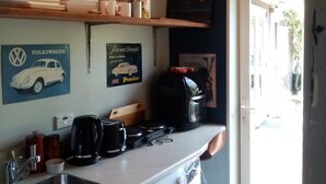 A kitchen with a sink, coffee maker, and a washing machine. There are shelves with dishes and a Volkswagen car poster.