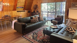Een gezellig blokhutinterieur met houten afwerking, een eethoek en een groot raam met uitzicht op de natuur.