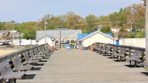 A wooden boardwalk with benches, a clock, and a building with a blue roof in the background. - Just steps away from the Boardwalk & Beaches, Walkable to Entertainment! (North Beach)