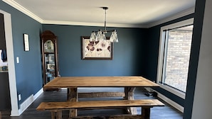 A dining area with a wooden table and bench, a chandelier, and a large window with a brick wall view. - Spacious 5-bedroom house in Green Bay with WiFi, 15 minutes to Packer stadium (Green Bay)