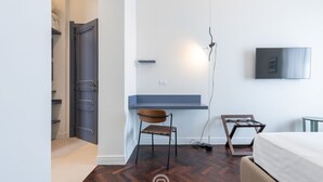 Une chambre à coucher moderne avec un lit, un bureau et une chaise, un téléviseur fixé au mur et un plancher en bois.