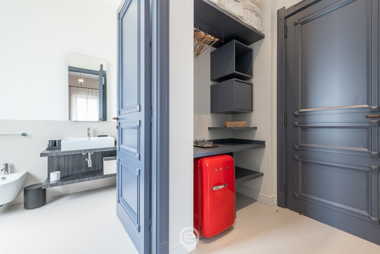 A modern bathroom with a white sink, dark vanity, and a red refrigerator.
