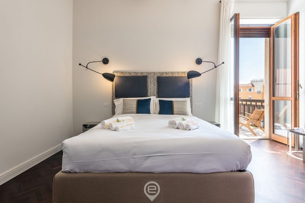 A neatly made bed with towels, a patterned headboard, and a view of the outside balcony.