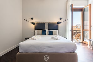 A neatly made bed with towels, a patterned headboard, and a view of the outside balcony.