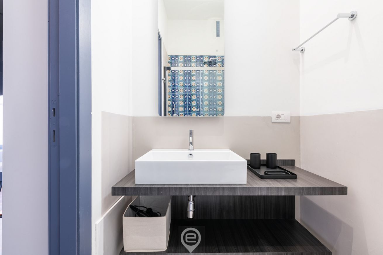 A modern bathroom with a white sink, dark wood vanity, and a blue patterned shower enclosure.