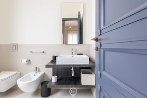 A modern bathroom with a white sink, bidet, and toilet. - Verso Suites Cagliari (Cagliari)