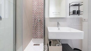 Une salle de bain moderne avec un lavabo blanc, un miroir et un espace douche agrémenté de carreaux à motifs.
