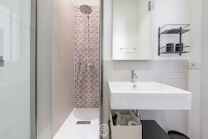 A modern bathroom with a white sink, a mirror, and a shower area with patterned tiles.