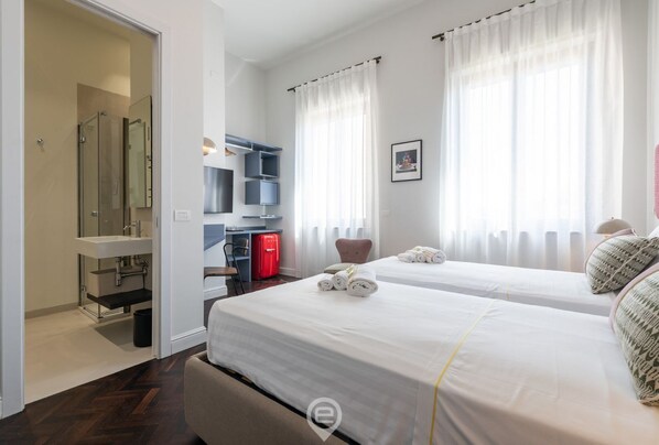 Habitación de hotel con dos camas, un escritorio, un mini bar rojo y zona de ducha.