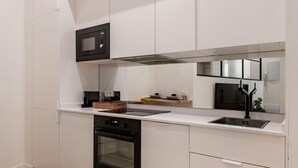 A modern kitchen with white cabinetry, a built-in oven, a microwave, and a stainless steel sink. - Charming Almudena I - (Madrid)