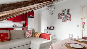 A modern living room with a sofa, a dining table set with plates and glasses, and a kitchen area with red cabinets. - La Latina Vibes - Apartment in the City Center (Madrid)