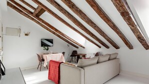 A modern loft with exposed wooden beams, a sofa, a dining table, and a TV. - La Latina Vibes - Apartment in the City Center (Madrid)