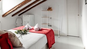 A bedroom with a sloped ceiling, a bed with a red blanket, a white dresser, a white wardrobe, and a white door. - La Latina Vibes - Apartment in the City Center (Madrid)