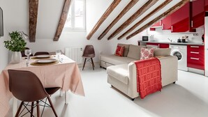 A modern loft apartment with exposed wooden beams, a dining area with a striped tablecloth, a sofa with a red throw, and a red kitchen. - La Latina Vibes - Apartment in the City Center (Madrid)