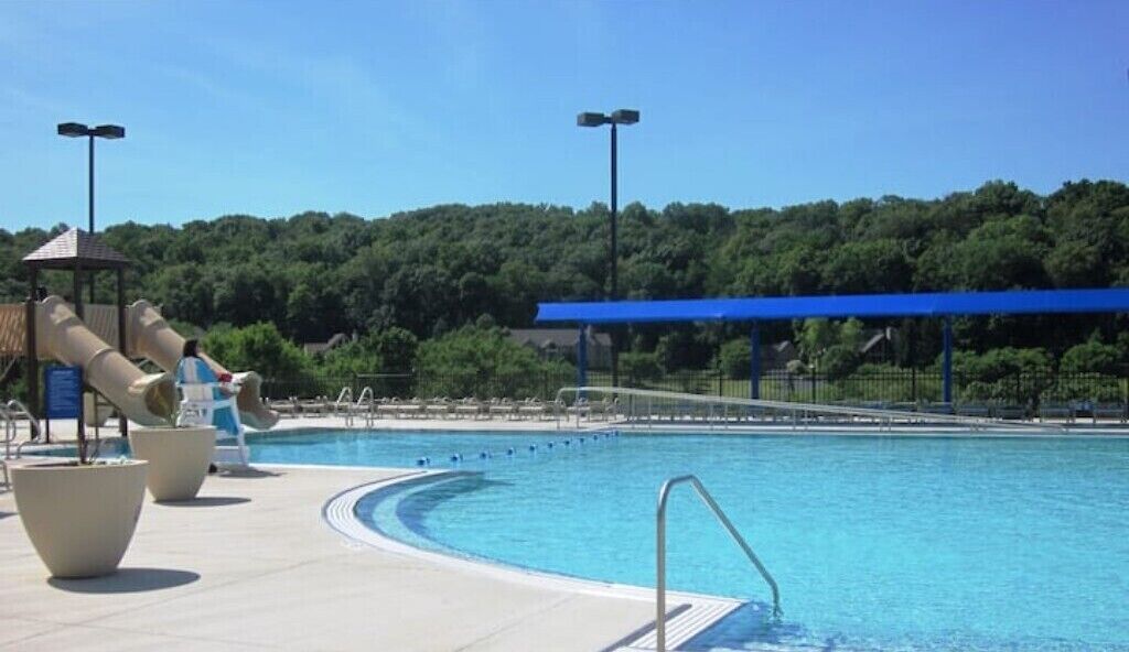 A swimming pool with slides, a covered area, and a forested hill in the background.