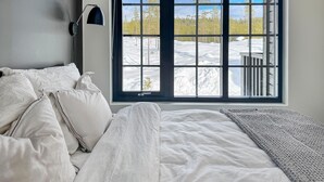 A bedroom with a large window, a bed with white bedding, and a view of a snowy landscape.