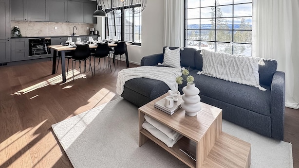 A modern living space with a grey sofa, a wooden coffee table, and a view of a snowy landscape through large windows.