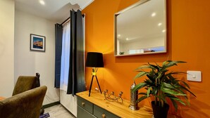 Ein Zimmer mit einem Holzkasten, einem Spiegel, einer Lampe, einer Pflanze und einem Stuhl.