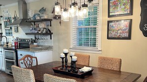 Une salle à manger avec une table en bois, des chaises en osier et des lampes suspendues.