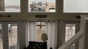 Une pièce dotée d’une grande fenêtre donnant sur un lac, d’un ventilateur de plafond et d’une pancarte sur laquelle on peut lire : « La vie est plus belle au bord du lac. »