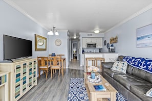Ein Wohnzimmer mit Flachbildfernseher, Holzmöbeln, einem gemusterten Teppich und einem Ledersofa mit nautisch inspirierten Kissen.