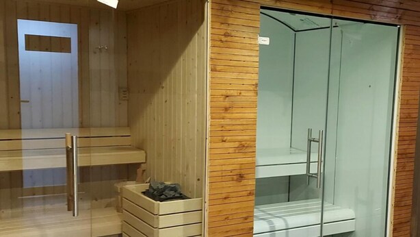 A modern room with a wooden wall, a glass shower enclosure, and a small wooden bench with a trash bin. - El Ghanami Hotel (Algiers)