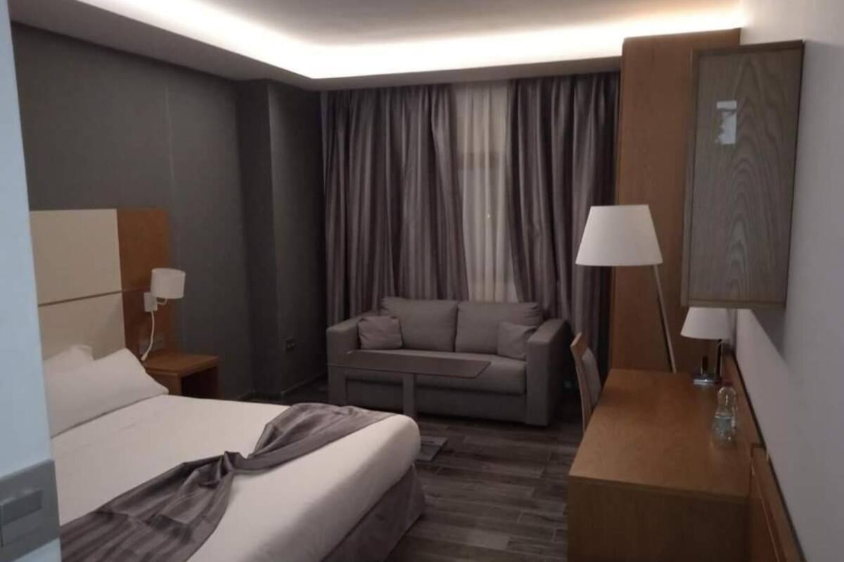 A hotel room with a bed, a sofa, a desk, and a lamp.