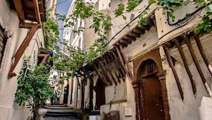 A narrow street with buildings on either side, featuring stone walls and wooden doorways. - El Ghanami Hotel (Algiers)