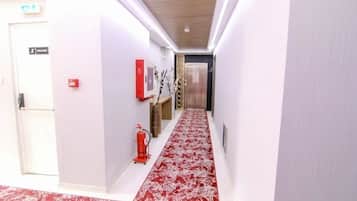 A hallway with a red patterned carpet, a fire extinguisher, a red emergency exit sign, and a door labeled "ESCALER".