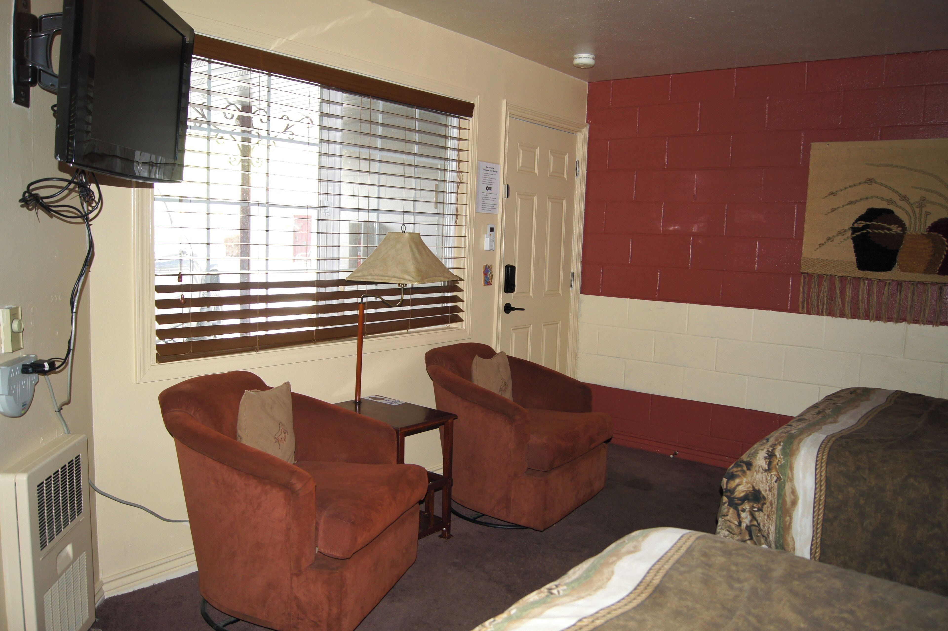 A room with two brown armchairs, a small table, a television mounted on the wall, and a door with a sign.