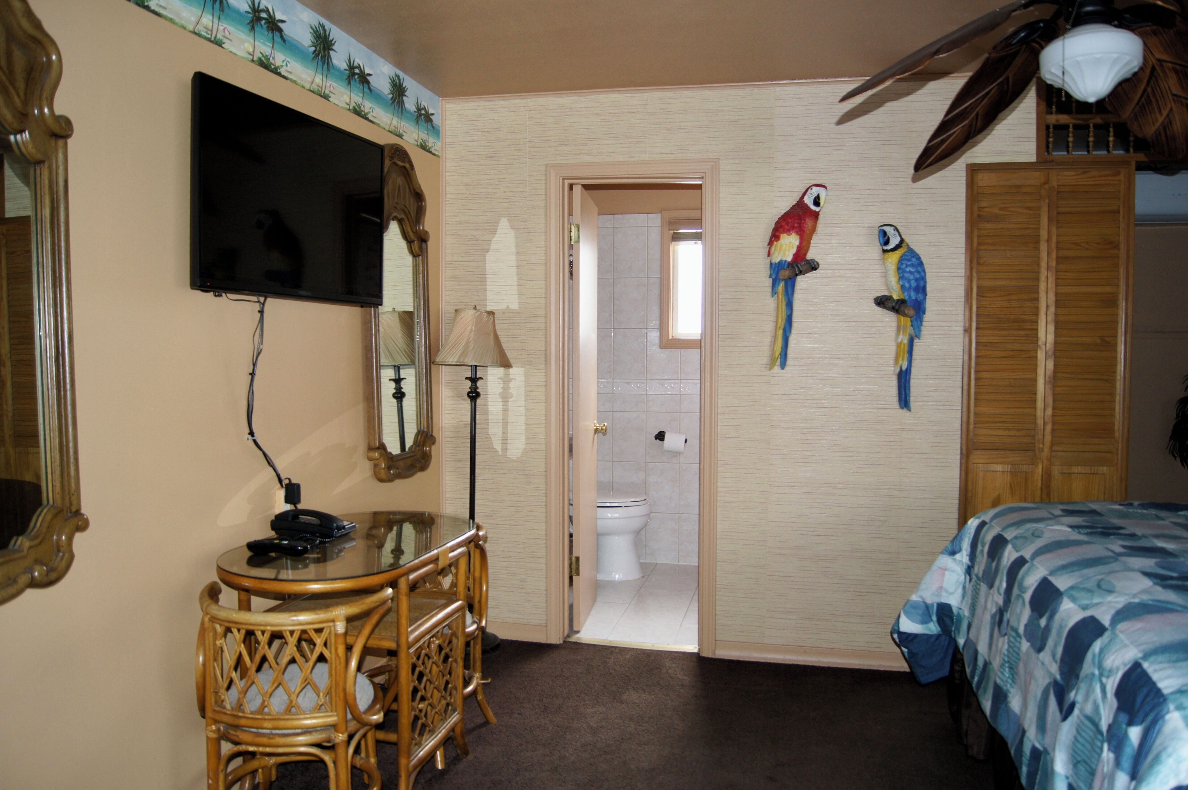 Una habitación de hotel con televisión, un escritorio con lámpara, una cama con cubrecama azul y dos loros colgados en la pared.