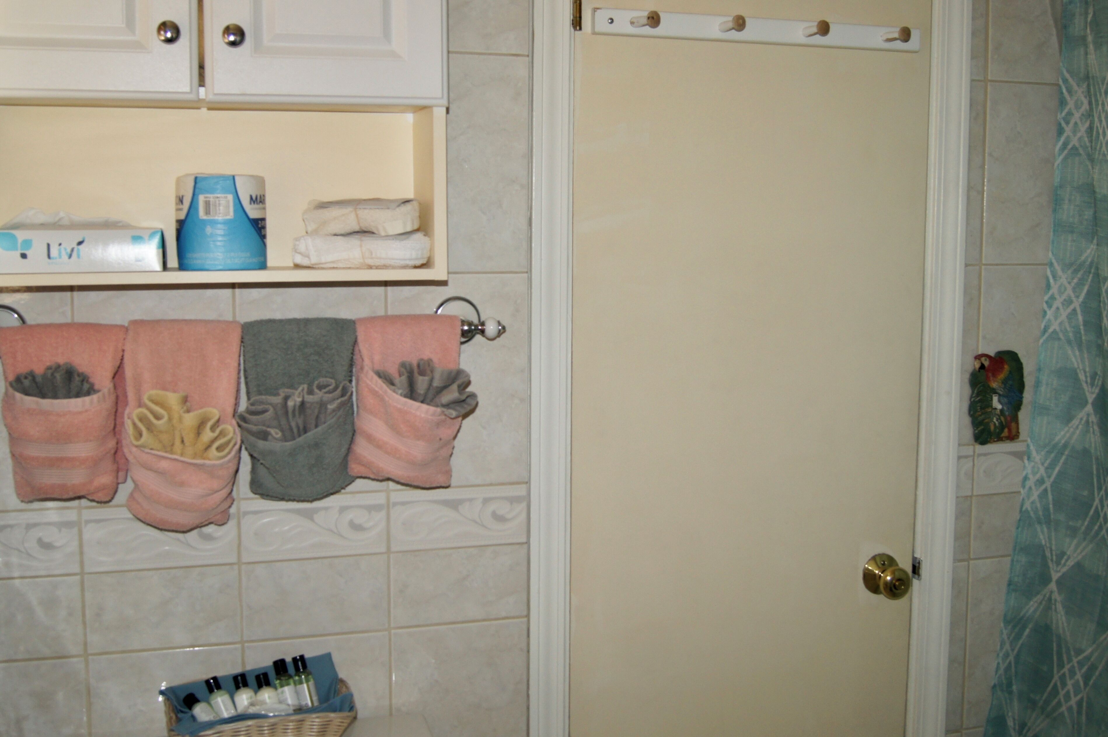 A bathroom with a toilet paper holder, a basket of toiletries, and towels hanging on a rack.