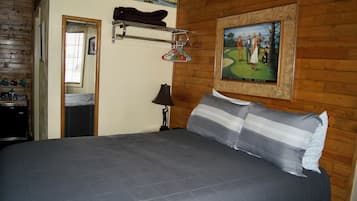 A bedroom with a large bed, wooden walls, a framed picture, and a coat rack with hangers.