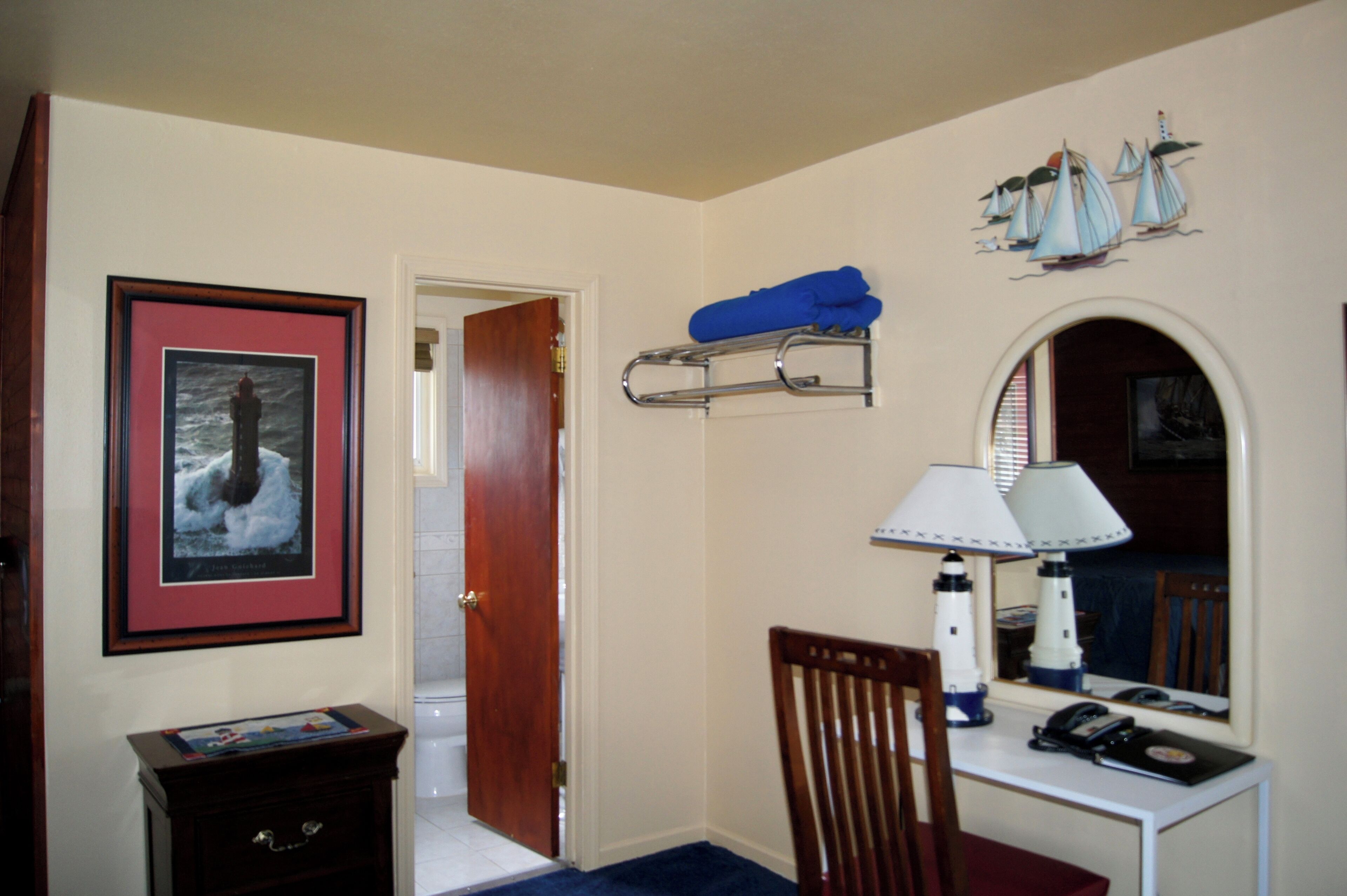 A hotel room with a desk, chair, lamp, and a framed picture on the wall.