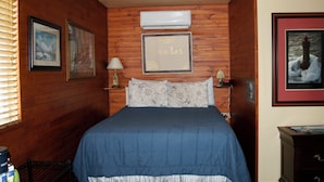 Una habitación con paneles de madera, una cama, cuadros enmarcados, un aire acondicionado y una lámpara.