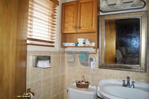 Een badkamer met toilet, wastafel, houten kastjes, een spiegel en een raam met zonwering.