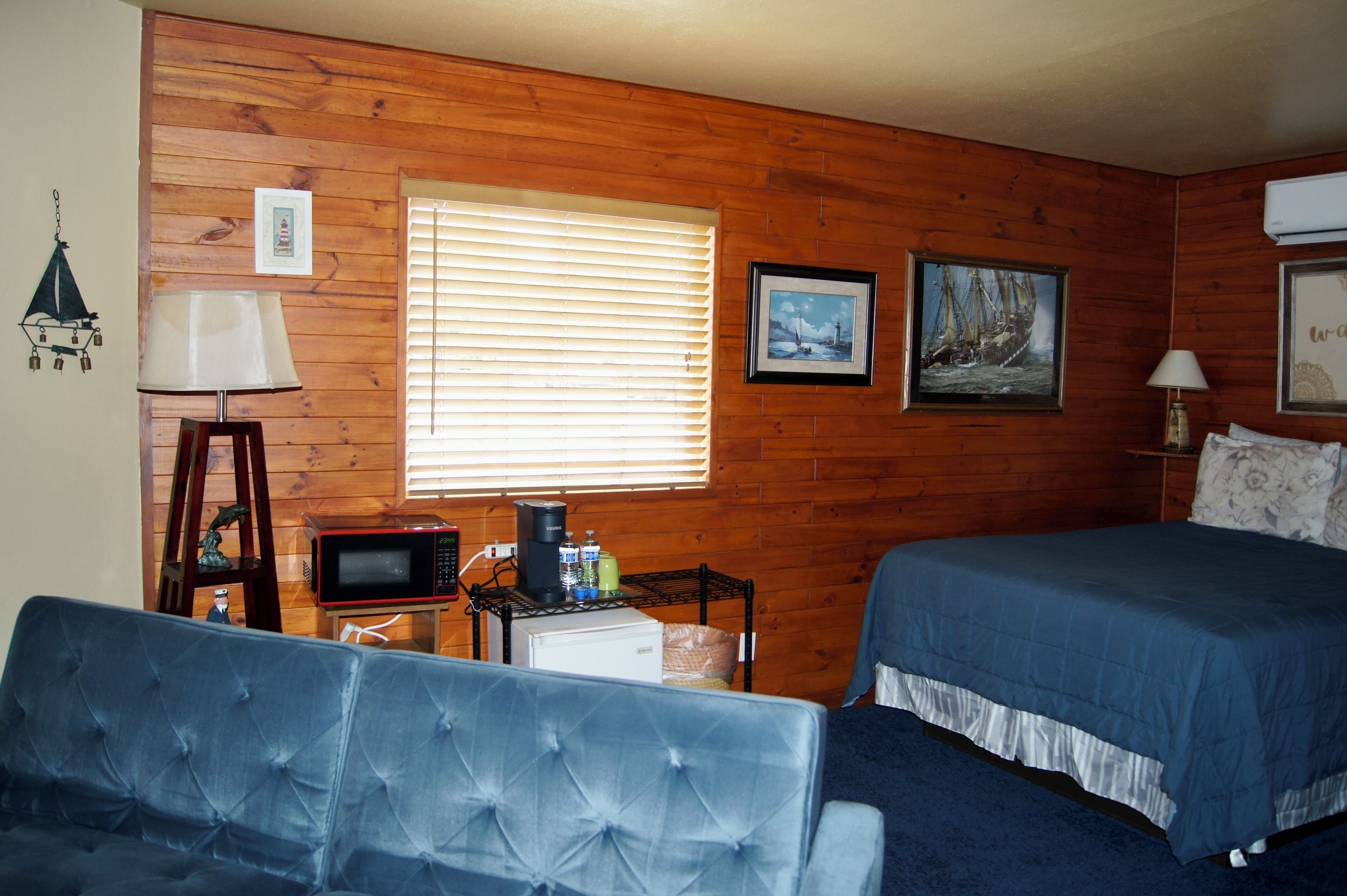 Une pièce aux murs en bois, un lit avec une literie bleue, un canapé bleu, une petite table avec un four à micro-ondes et un cadre photo accroché au mur.