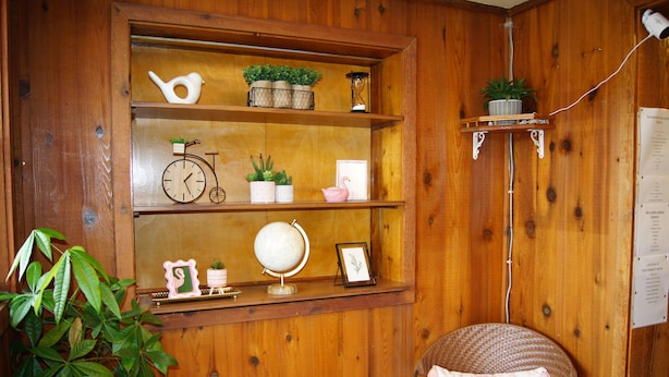 Un interior de madera con una repisa que muestra un reloj, plantas, un globo terráqueo y un cuadro enmarcado.