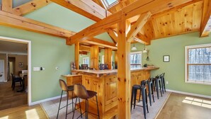 Une cuisine spacieuse avec des poutres en bois, un îlot central doté de tabourets et une vue sur l’extérieur grâce à une grande fenêtre.