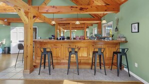 Une cuisine avec un bar en bois et trois tabourets, une fenêtre et une porte.